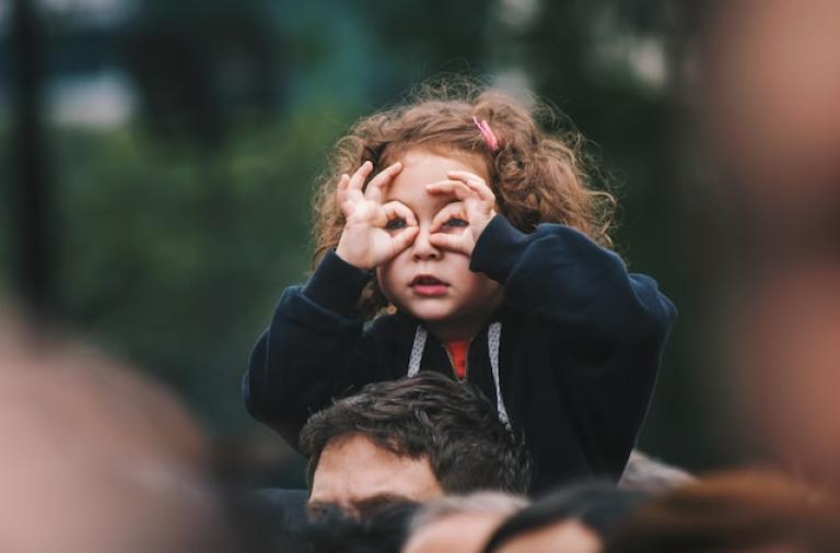 little girl on the shoulders of her father looking over a crowd