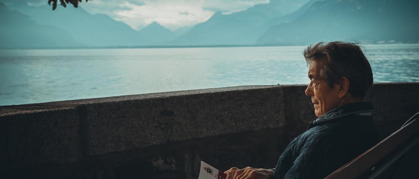 Man reading a book, sat down overlooking a lake at sunset