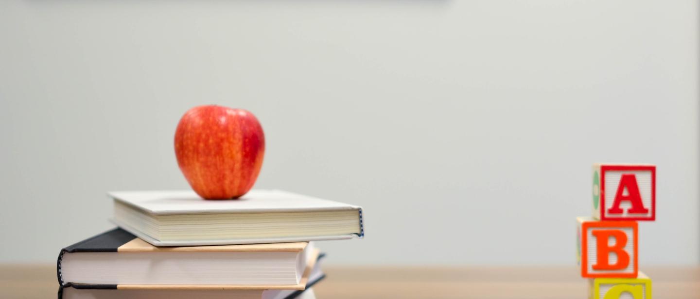 Desk with books and an apple on top of the books in a classroom