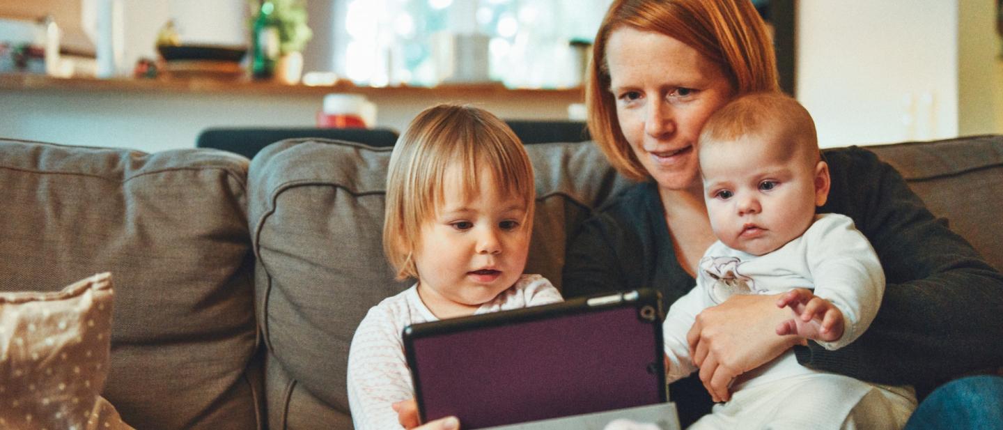 mother with her two young children reading together on a tablet device