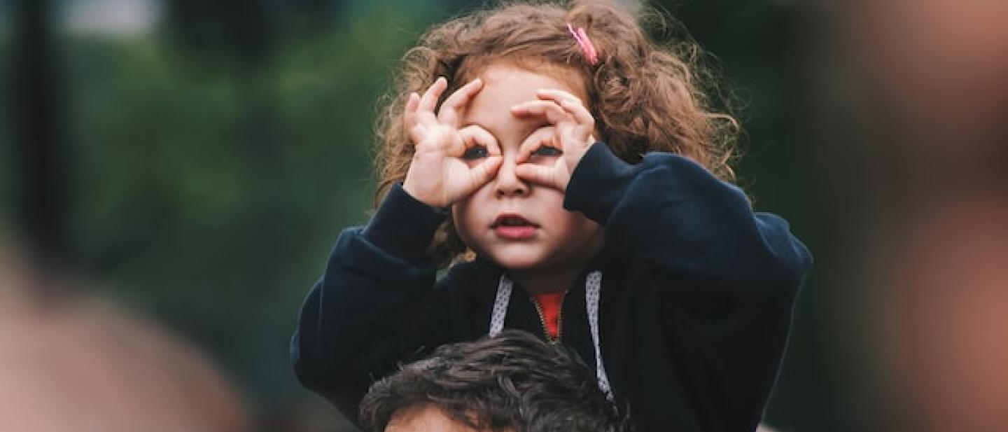 little girl on the shoulders of her father looking over a crowd